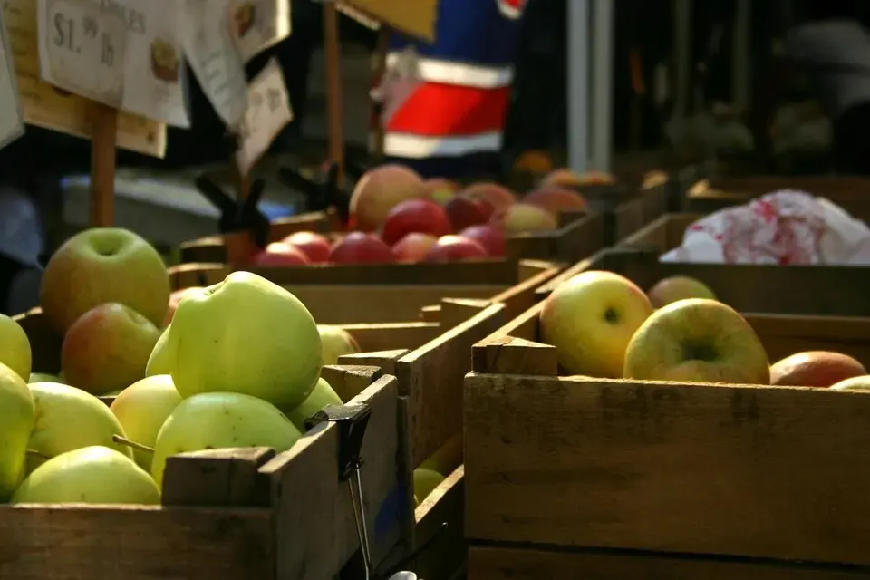 Des pommes jaunes et rouges rangées dans des cagettes en bois sur l'étal d'un marché, des étiquettes de prix en arrière-plan