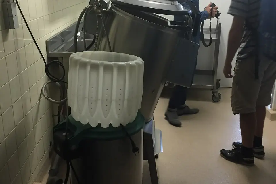 Dans la cuisine d'une cantine scolaire carrelée de blanc, deux personnes de dos observent un grand appareil de préparation en inox