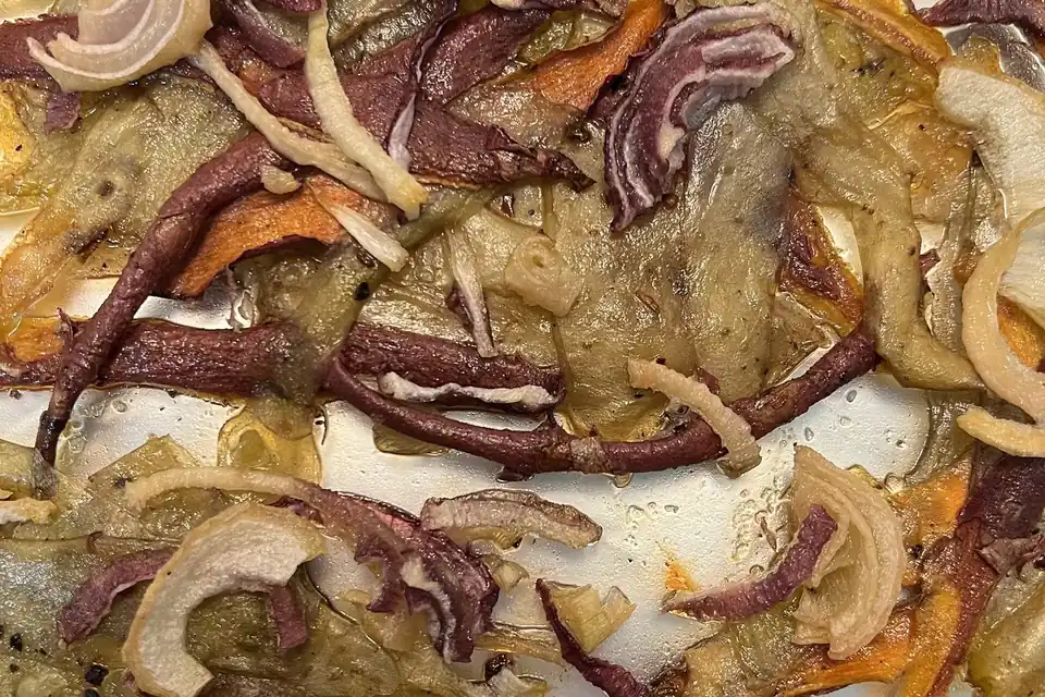 Des épluchures de pommes de terre, de patates douces et des oignons, rôtis et dorés sur une plaque de cuisson