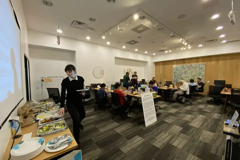 Une salle de travail où une douzaine de personnes sont penchées sur des ordinateurs portables, autour de tables disposées en îlots