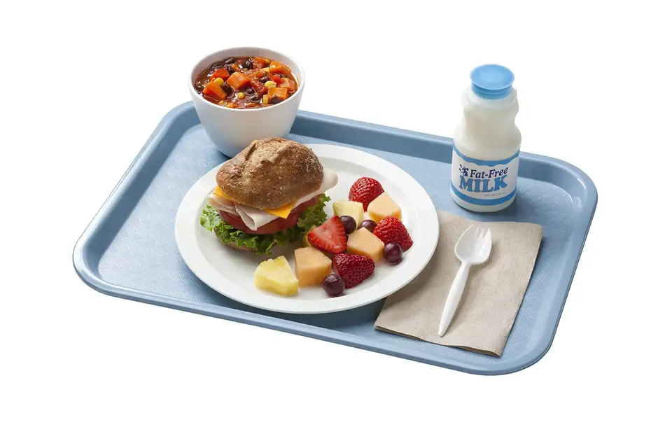 Un plateau-repas scolaire avec un sandwich, une salade de fruits frais, une petite portion de légumes et une bouteille de lait