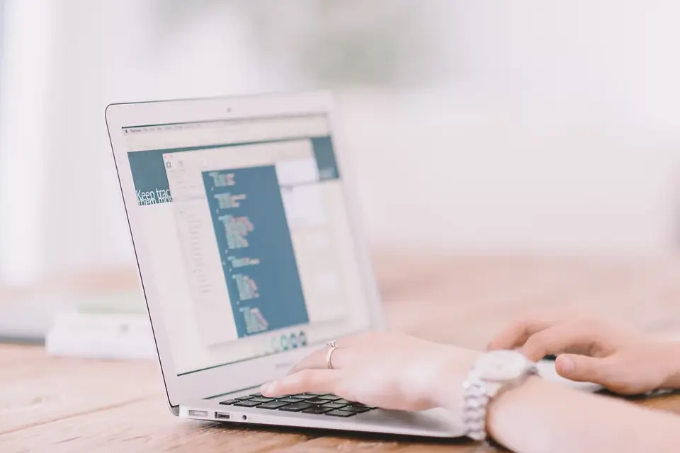 Deux mains posées sur le clavier d'un ordinateur portable ouvert sur un éditeur de code, sur une table claire
