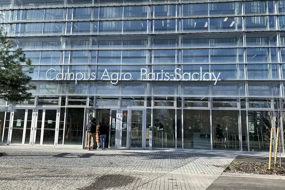 L'entrée d'un campus universitaire moderne, avec un parvis, des bâtiments vitrés et quelques arbres