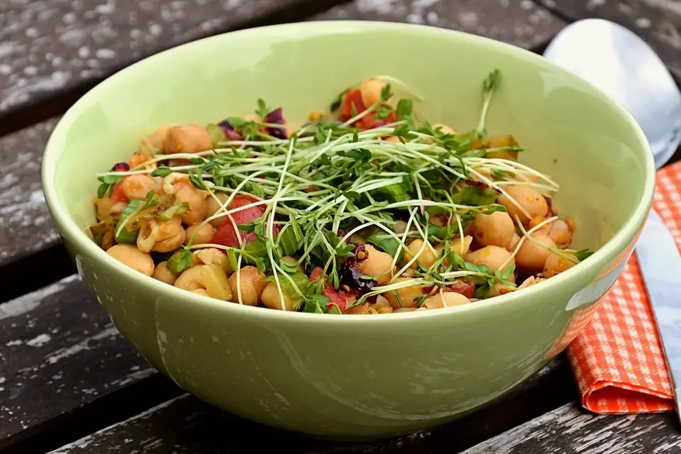 Un bol vert rempli d'une salade de pois chiches, de légumes et de jeunes pousses de cresson, posé sur une table en bois